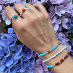 bracciale in acciaio silver con perle di fiume bianche abbinato con bracciali con perle azzurre e coralli rossi e anellino con perle di fiume e corallo quadrato elasticizzato