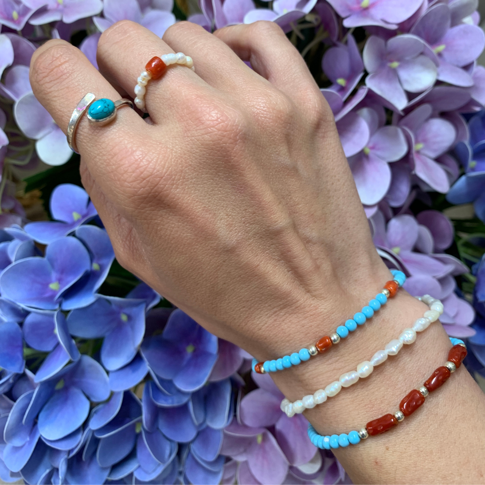bracciale in acciaio silver con perle di fiume bianche abbinato con bracciali con perle azzurre e coralli rossi e anellino con perle di fiume e corallo quadrato elasticizzato